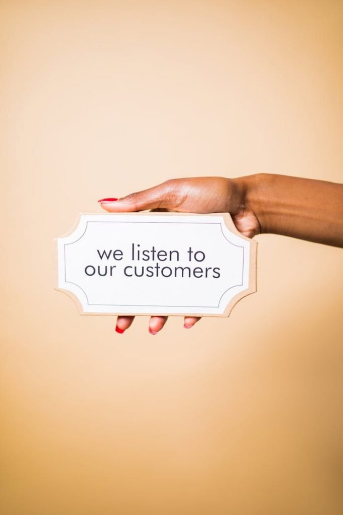 A hand holding a sign saying we listen to our customers on a neutral background.